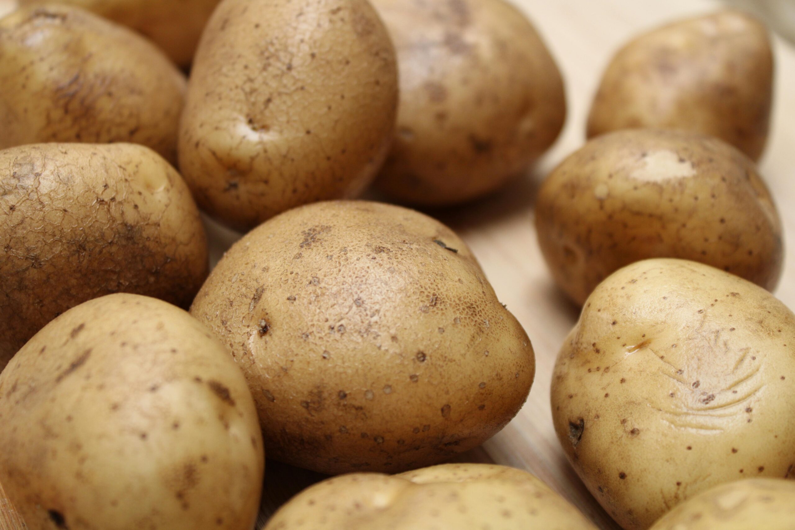 High-quality close-up photo of fresh raw potatoes on a wooden surface, ideal for food and culinary themes.